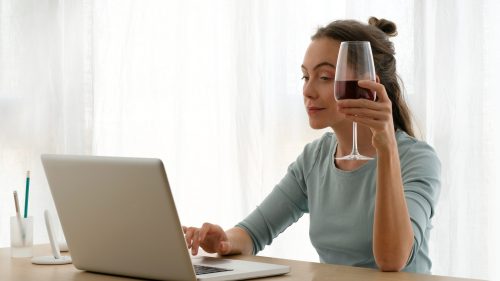 Woman working on a laptop with a glass of wine